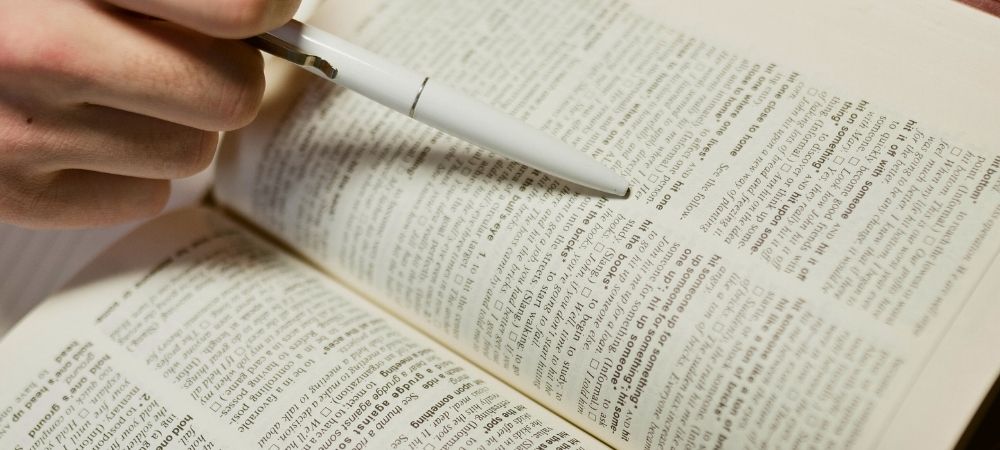 Een open woordenboek. Iemand wijst een woord aan met een pen.