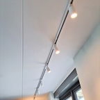 Witte opbouw spanningsrail met gemonteerde railverlichting en drie spots.