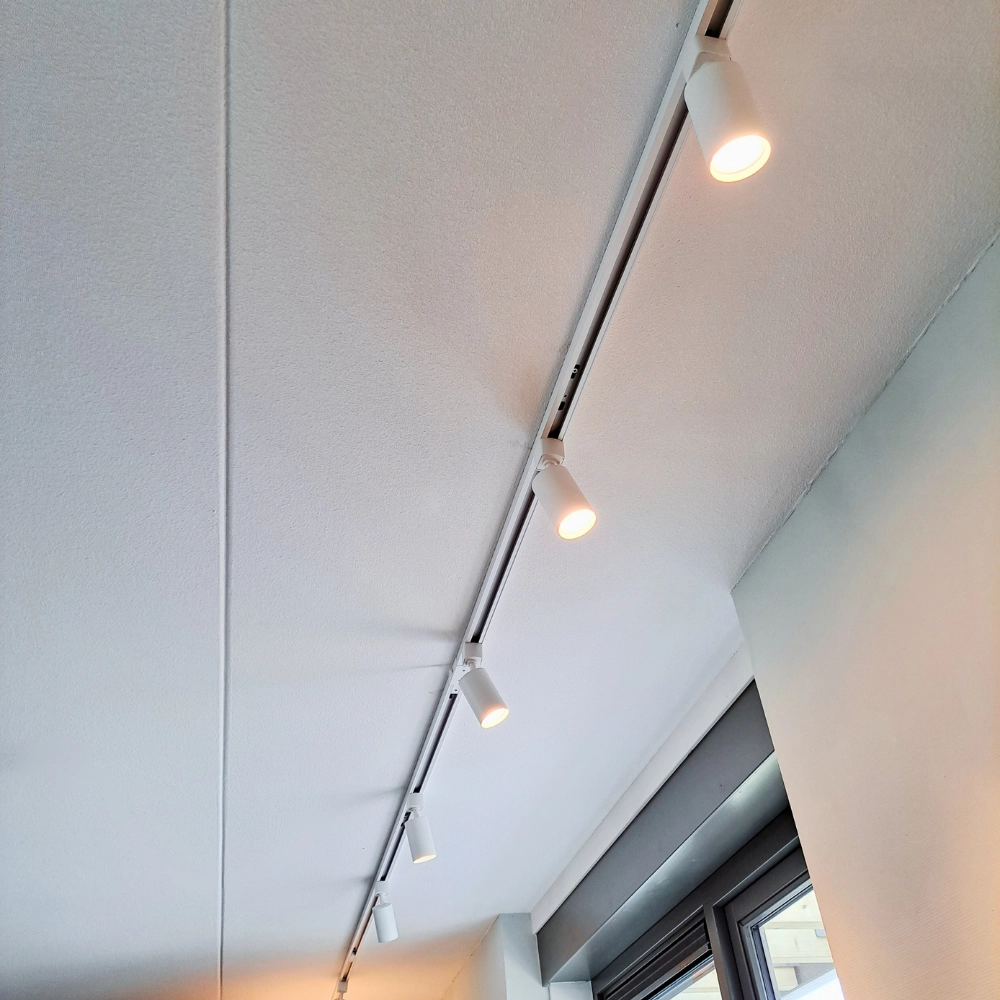 Witte opbouw spanningsrail met gemonteerde railverlichting en drie spots.