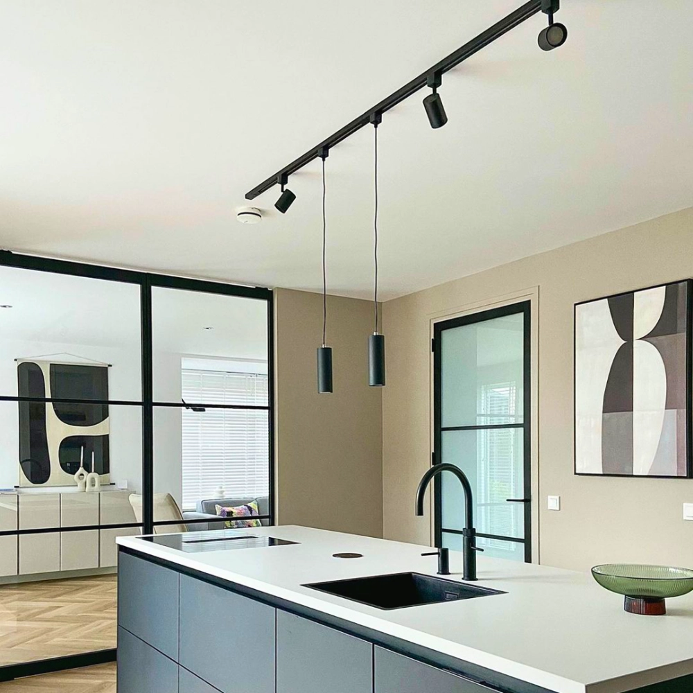 Zwarte spanningsrail aan plafond met drie zwarte railspots en kabels