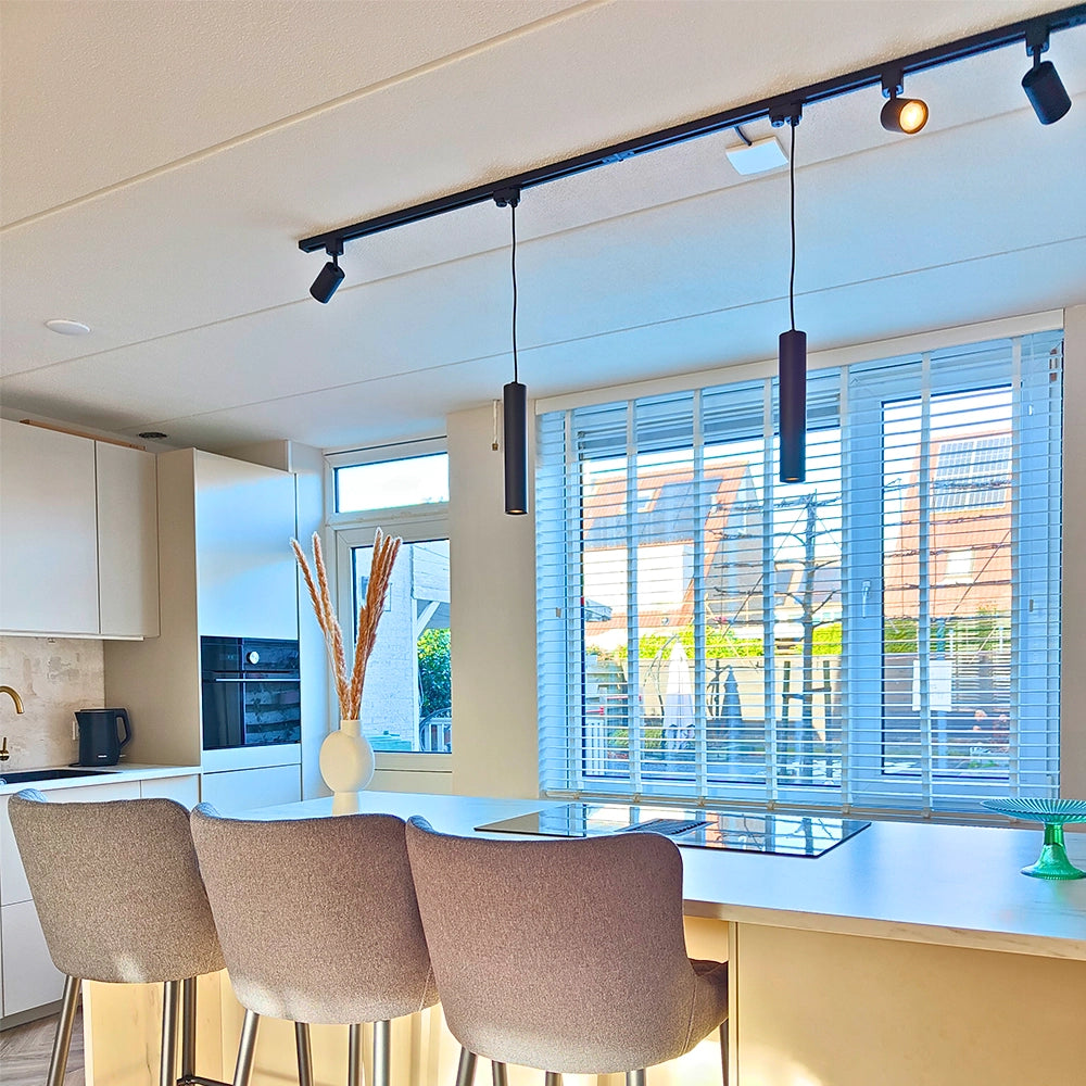 Zwarte railverlichting met drie spotkoppen en twee hangcilinders, warm verlichte lampjes.