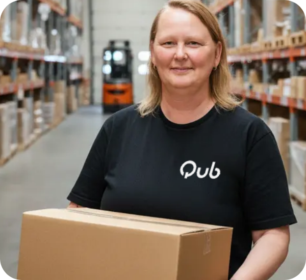 Een blonde vrouw staat in het magazijn. Ze heeft een shirt aan met 'Qub' erop en houdt een doos vast.